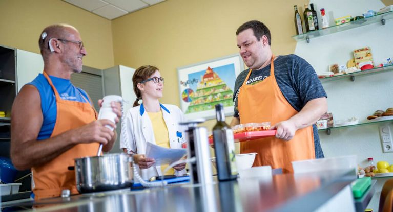 Patienten mit orangefarbenen Schürzen kochen gemeinsam mit einer Therapeutin