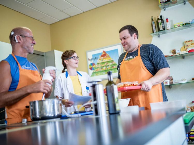 Patienten mit orangefarbenen Schürzen kochen gemeinsam mit einer Therapeutin