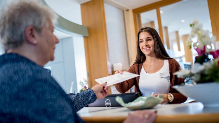 Die Rezeptionistin gibt einer Patientin eine Infobroschüre
